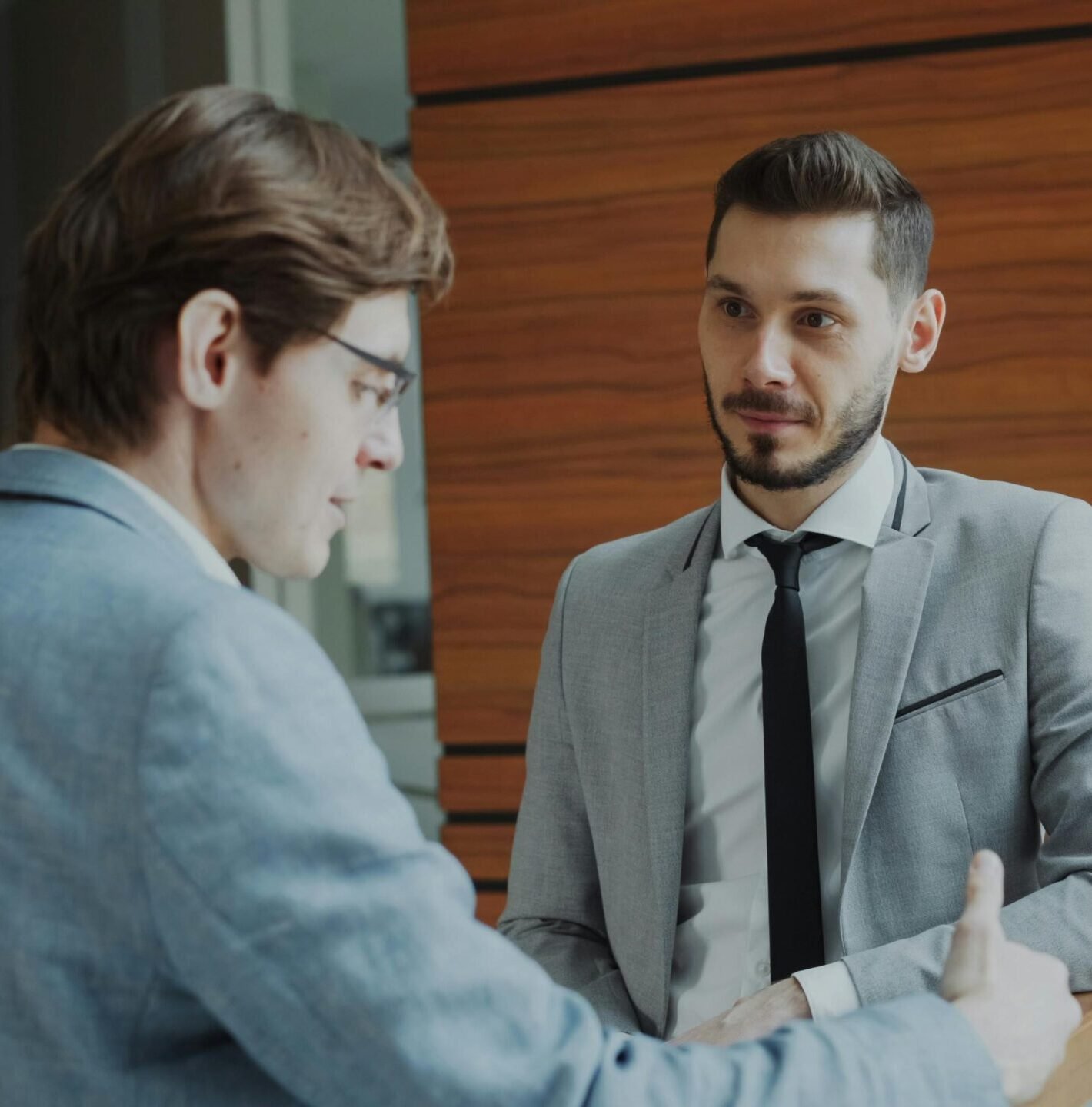 Two male professionals engaged in conversation in a modern office setting.
