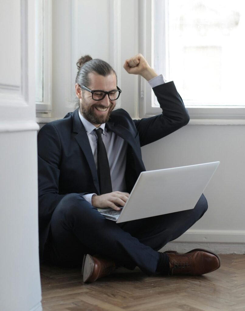 Cheerful man sitting on the floor with a laptop, celebrating work success.