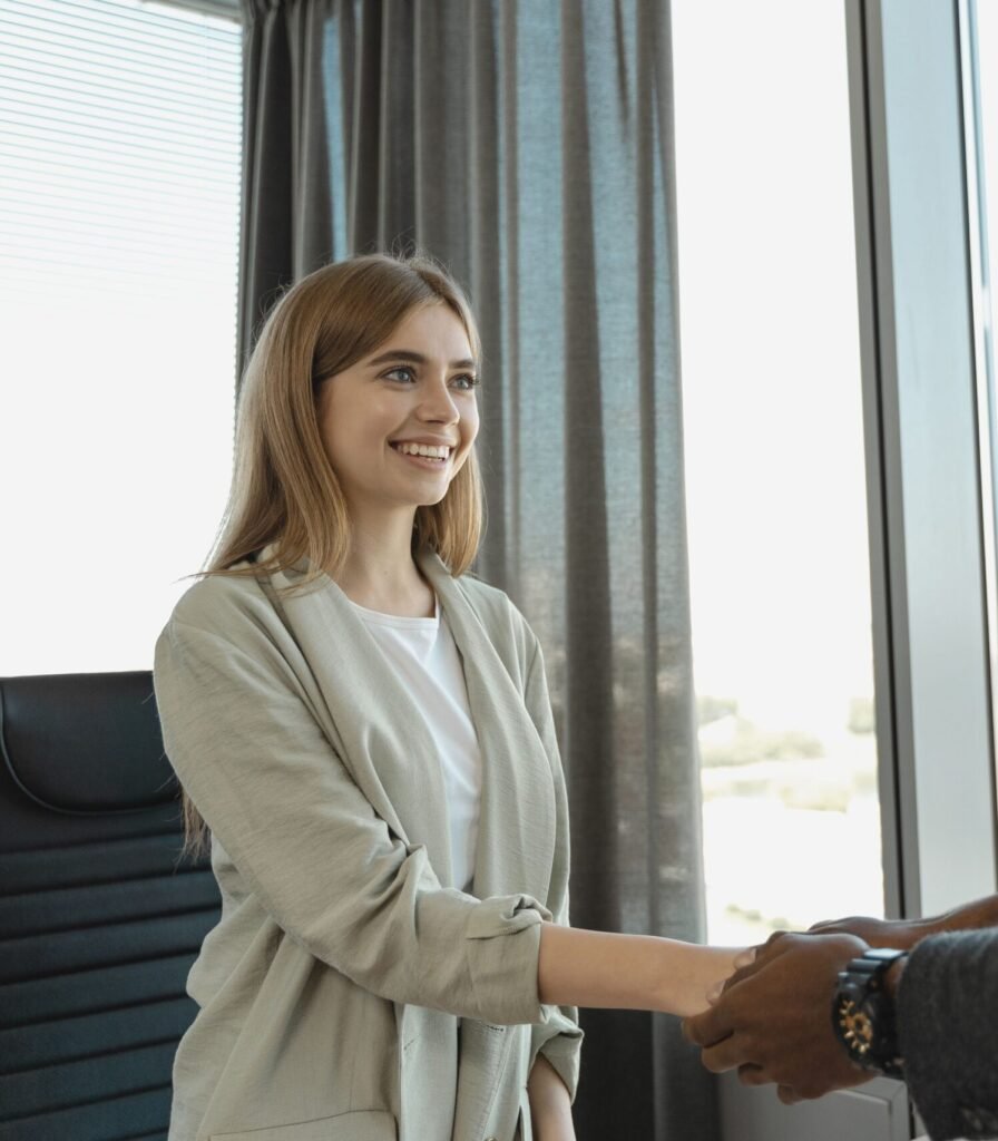 Woman smiling and shaking hands at a business office, signaling a successful job interview.